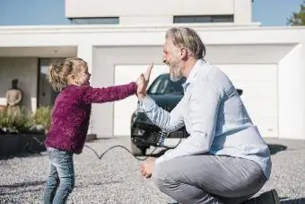 Glückliches Mädchen gibt seinem Vater an einem sonnigen Tag vor dem Auto High Five