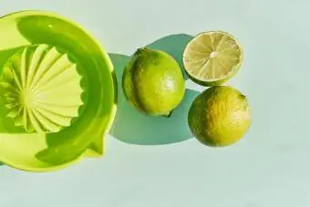 gröna citronlimefrukter och en juicepress för att pressa dem