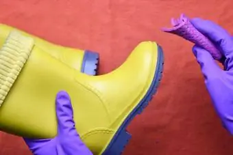 Vyras purpurinėmis guminėmis pirštinėmis valo vaikiškus geltonus guminius batus