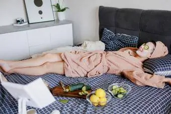 kvinne slapper av på sengen med agurk øyemaske for selvpleie