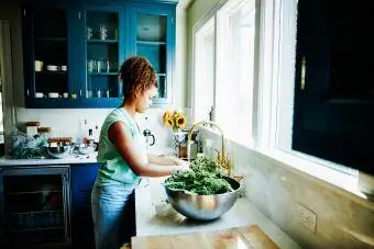 Grua që lan lakra jeshile organike në lavamanin e kuzhinës