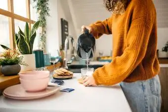 Fiatal nő teát főz egy elektromos vízforralóval a konyhájában