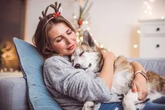 Noel maskesi takan ve köpeğini tutan kadınlar kanepede oturuyor