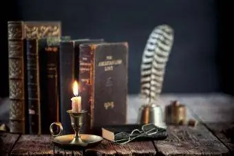 Studijų zona su senomis knygomis, plunksnakočiu ir senoviniu žvakidėliu ant seno medinio stalo