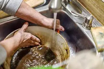 Verbrannte Speisereste aus der Dutch Oven-Kochpfanne schrubben