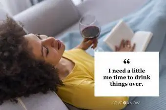 İçki içen kadın kitap ve bir kadeh şarapla kanepede dinleniyor.