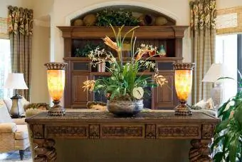 Magagandang inukit na console table na may silk plant at lighted fixtures sa isang den