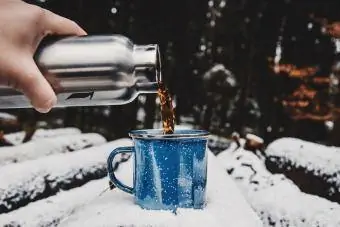 Tè Di Versamento Della Mano Ritagliata In Tazza Sul Registro Coperto Di Neve