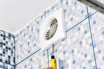 Man verwijdert het ventilatierooster in de badkamer met een schroevendraaier
