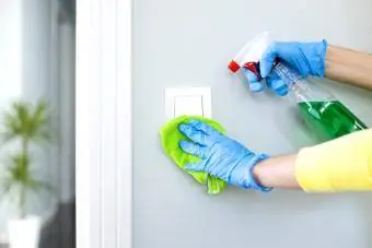 Mulher limpando um interruptor de luz com spray desinfetante