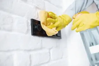 Koruyucu eldivenli kadın evini temizlerken duvar anahtarlarını dezenfekte ediyor