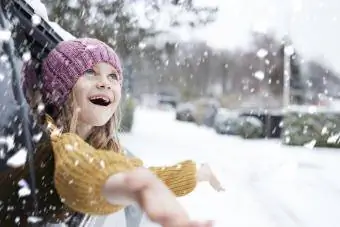 κορίτσι που γέρνει έξω από το παράθυρο του αυτοκινήτου πιάνει νιφάδες χιονιού