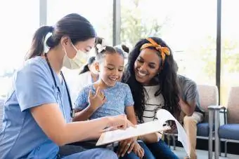 Medicinska sestra i djevojka gledaju medicinski karton dok se žena smiješi