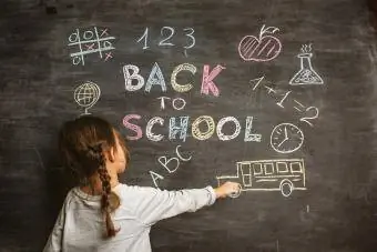 Mała dziewczynka pisze na tablicy „Powrót do szkoły”.