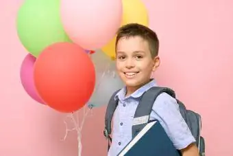 Uczeń z plecakiem trzyma książkę i wielokolorowe balony