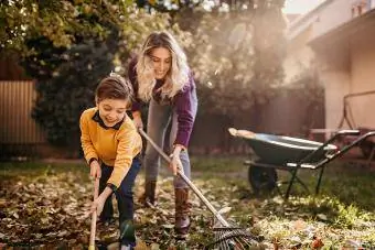 แม่และลูกชายเล่นในสวนหลังบ้านเพื่อทำความสะอาดใบไม้ในฤดูใบไม้ร่วง