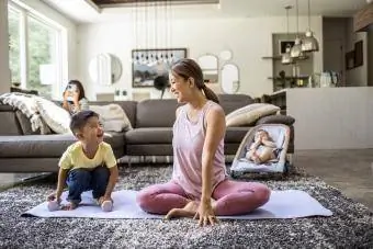 Nëna duke bërë joga në shtëpi e rrethuar nga fëmijë