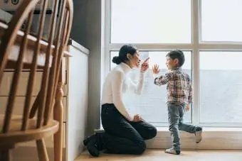 Māte un dēls kopā sarunājas pie lielā dzīvokļa loga