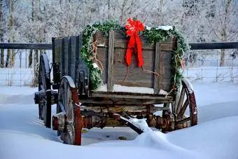 Staromodna drvena kolica s božićnim ukrasima stoje u snijegu