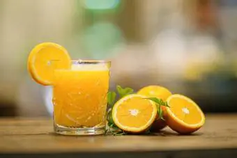 Свежий апельсиновый сок рядом с кусочками апельсина