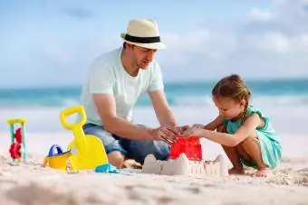 baba ve kızı sahilde kumdan kale inşa ediyor
