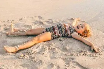 batang babae na gumagawa ng sand angel sa beach