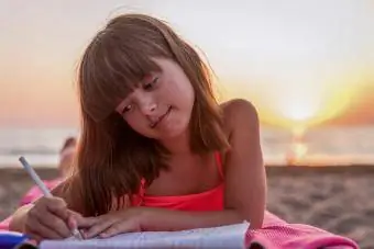 niña escribiendo en un diario en la playa