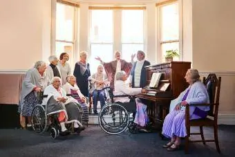 Bir grup yaşlı kadın birlikte şarkı söylüyor ve bir huzurevinde piyano çalıyor
