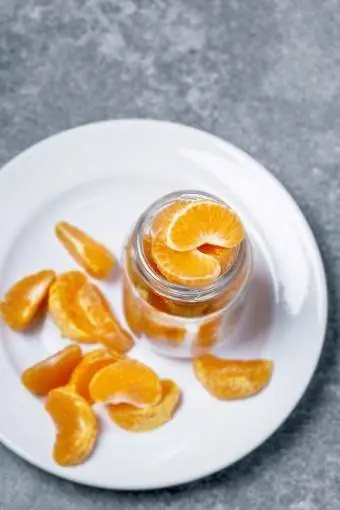 Segmen clementine yang dikupas pada toples dan piring putih