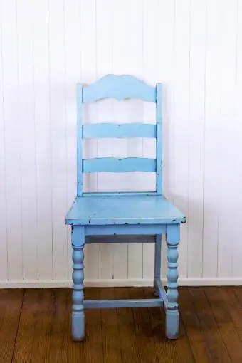 Stare krzesło z niebieską drabinką na tle białej ściany