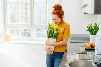 Wanita muda tersenyum berdiri dan melihat ke bawah pada buket tulip