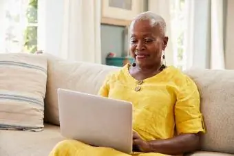 Grua e moshuar në divan duke përdorur laptop