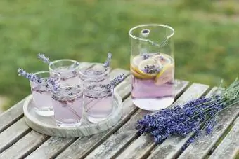 Koktail Lavender Lemonade dihiasi dengan bunga di atas meja kayu di luar ruangan