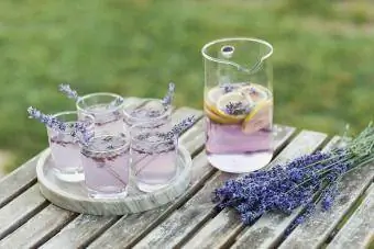 Còctel de llimonada de lavanda decorat amb flors sobre taula de fusta a l'aire lliure