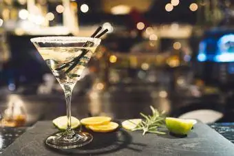 Copo de martini sobre superfície polida com rodelas de limão e alecrim