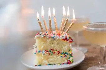 Свечи горят на кусочке торта с брызгами возле шампанского