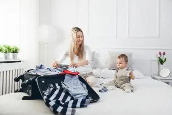 Glad mor med barnet sitt som pakker klær til ferie