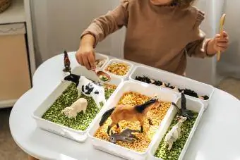 Niña jugando con animales de granja en un contenedor sensorial