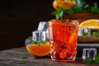 Mezcal Negroni kokteilis kristāla glāzēs ar apelsīna šķēlīti un svaigiem neapstrādātiem apelsīniem