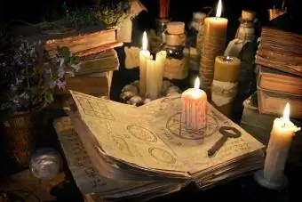 Krvava sveča z rustikalnim ključem na knjigi čarovnic v soju sveč