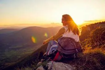 wanita tersenyum duduk di puncak gunung