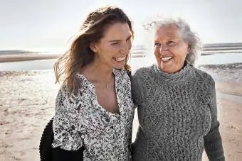 voksen datter ler og går på stranden med eldre mor