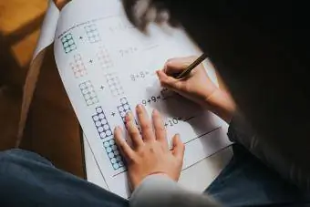 ბავშვი ამატებს ნომრებს საშინაო დავალების დაბეჭდილ მათემატიკურ ფურცელზე
