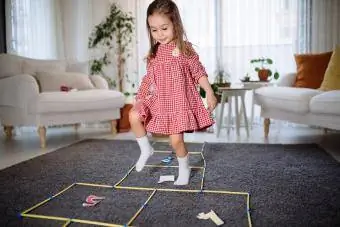 Nena infantil activa i somrient que es diverteix s altant, jugant a la rayuela a casa