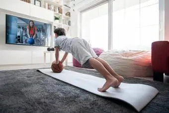 صبي صغير في المنزل يمارس التمارين ويشاهد مدربًا عبر الإنترنت