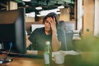 Unavená podnikateľka s hlavou v ruke sedí za počítačovým stolom v kancelárii
