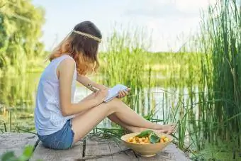 Teenager sitzt auf einer Brücke in der Nähe von Wasser und schreibt auf ein Notizbuch