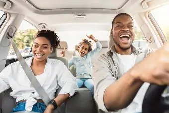 Familje e lumtur me tre persona që këndojnë duke u argëtuar me makinë