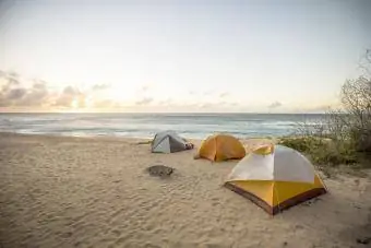 Drie tenten opgezet in het zand met de ondergaande zon in de verte