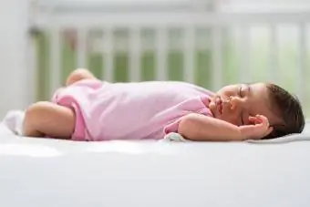 bayi perempuan memakai onesie merah jambu tidur di buaian
